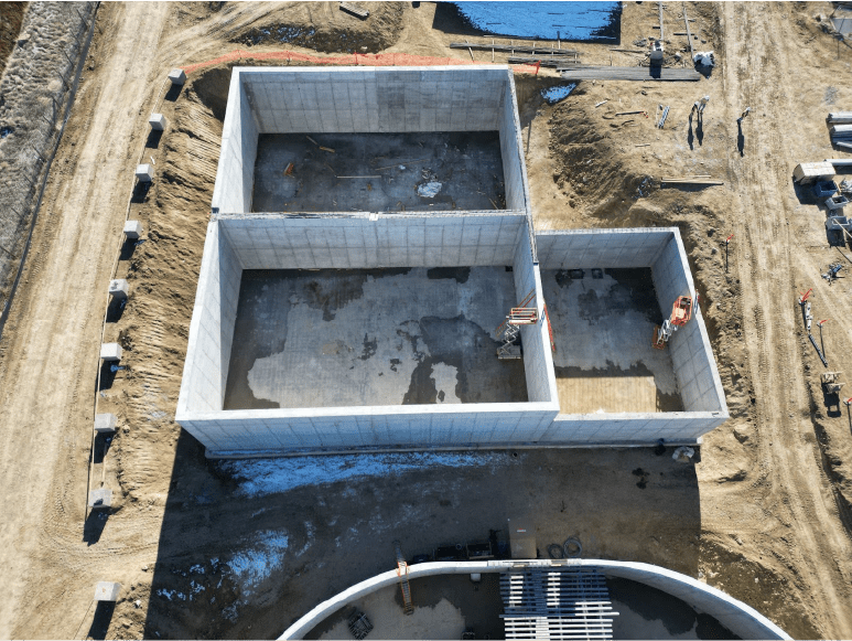 An aerial view of a construction site showing two large rectangular concrete tanks, partially complete. The walls of the tanks have been poured, and finishing touches are being added in preparation for water testing.