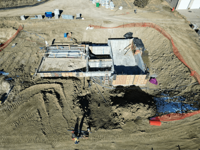 Construction progress at the Headworks site showing newly built walls, poured concrete slabs, and an excavated work area surrounded by safety barriers.