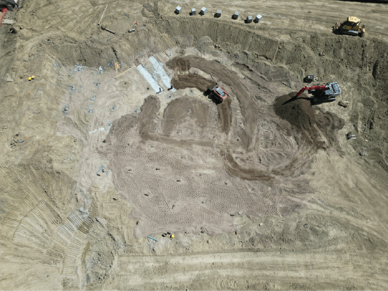 Aerial view of a construction site featuring a dirt pit, highlighting piers being drilled for a solid foundation of an oxidation ditch.