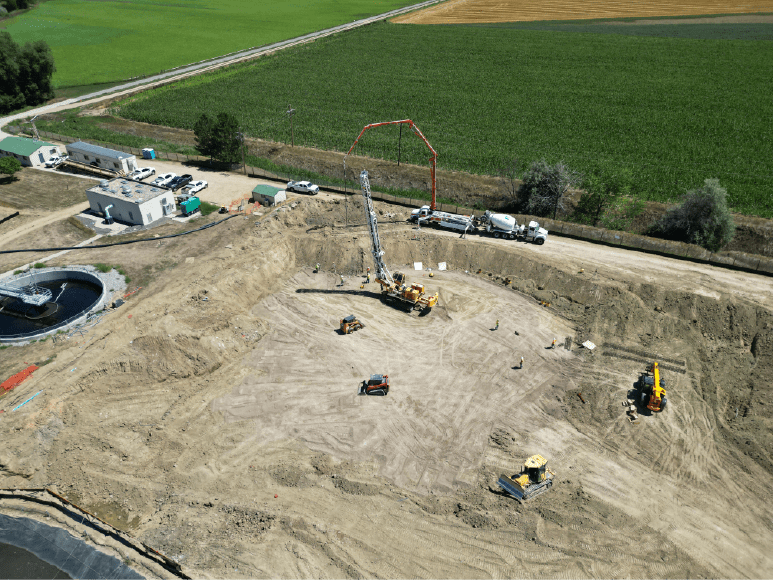 Aerial perspective of a construction site showcasing equipment, completed piers ready for rebar, and the initial slab pour.