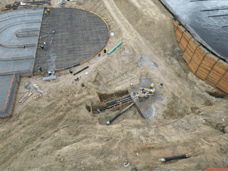 Aerial image of a construction site with a large building, emphasizing the installed inlet and outlet pipes for water treatment.