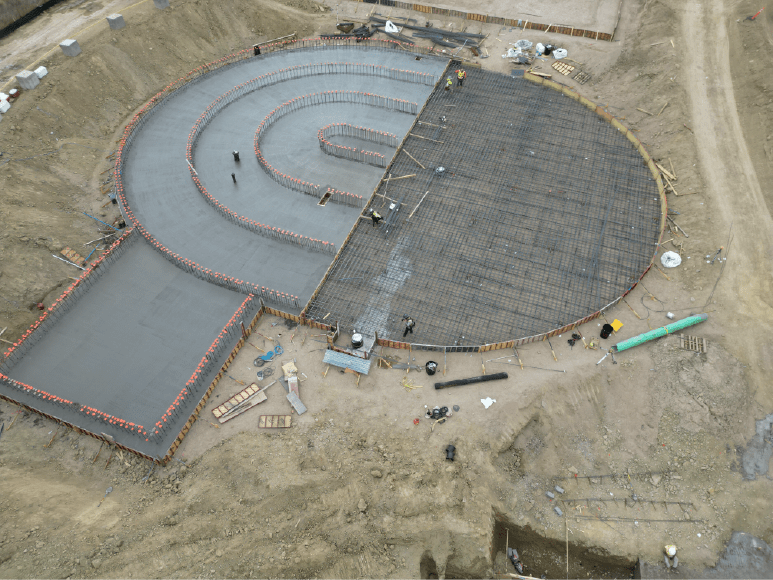 Aerial view of a concrete plant showcasing the oxidation ditch with rebar and half of the slab poured, highlighting a large cement pour.