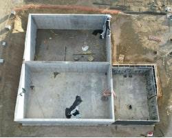 Aerial view of the construction progress on the aerobic digester and dewatering building, showing nearly completed poured concrete walls and a clean worksite.