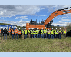 A team of individuals positioned in front of a large excavator, representing breaking ground for the new Niwot Sanitation District plant construction.