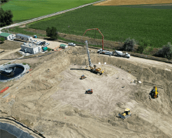 Aerial image of a construction site with machinery, highlighting finished piers for rebar and the first slab pour for the oxidation ditch.