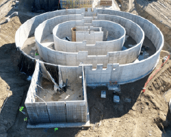 An aerial view of the construction site showing the Oxidation Ditch anaerobic tank taking shape, featuring circular concrete walls, rebar installations, and surrounding construction activity.